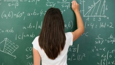 Woman with back turned, writing price and math on black board