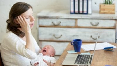 woman working from home on computer with upset baby in arms