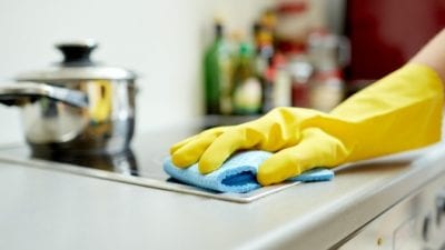How Much to Clean 5 Rooms close-up of hand cleaning stovetop with microfiber cloth